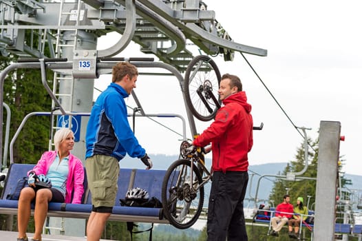 Man helping young couple taking down bicycle from chair lift