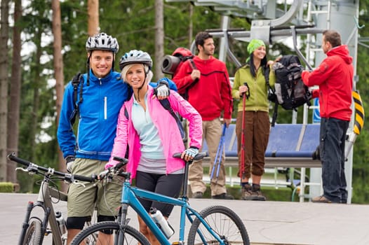 Smiling mountain bikes couple and hikers waiting after chair lift trip