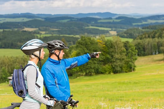 Sporty cyclist couple, man pointing to beautiful landscape