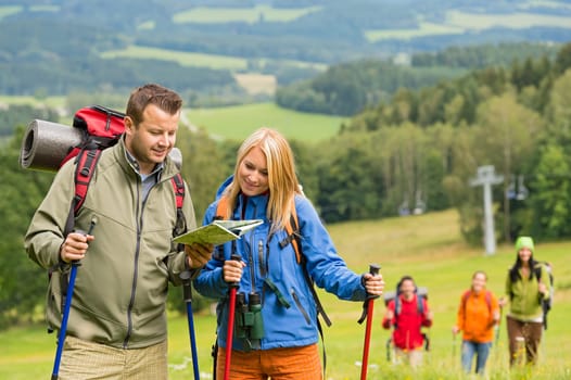 Young hiking couple with friends looking map to find track