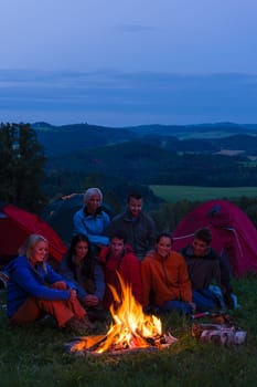 Friends watching fire together beside camp and tents in dark
