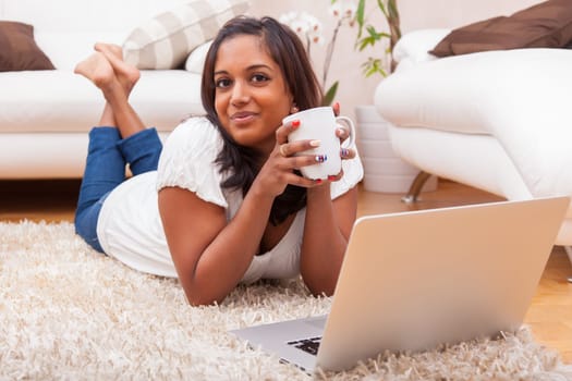 Young happy indian lying down on the floor woman using a laptop
