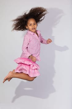 Portrait of cute Young African American girl jumping, over gray background
