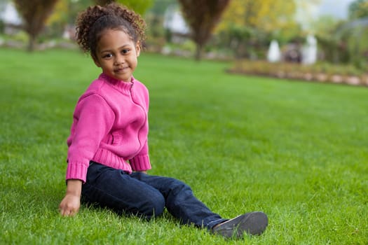Outdoor portrait  of a cute little African Asian girl lying seated on the grass