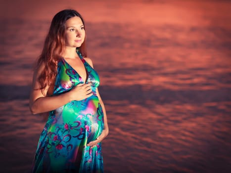 Beautiful pregnant woman at sunrise near the sea