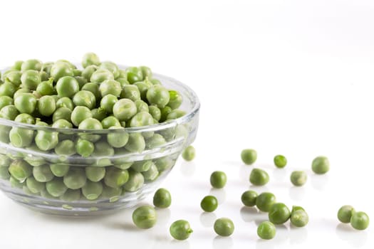 Fresh green peas in a glass bowl and on white surface.
