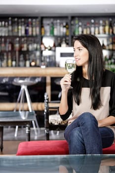 Attractive young woman enjoying a glass of white wine in a wine bar.