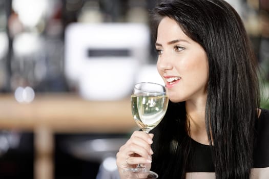 Attractive young woman enjoying a glass of white wine in a wine bar.