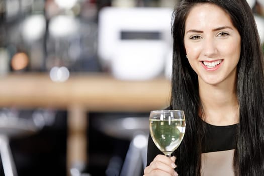 Attractive young woman enjoying a glass of white wine in a wine bar.