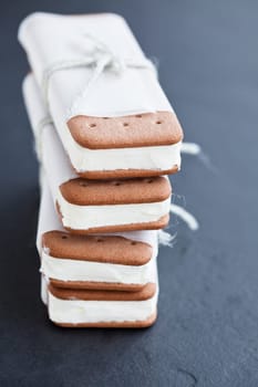 Closeup of stack of vanilla ice cream biscuits wrapped in white paper with string and bow on dark background
