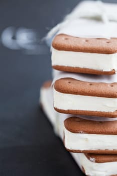 Closeup of stack of vanilla ice cream biscuits wrapped in white paper with string and bow on dark background