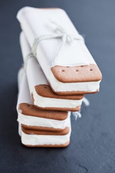 Closeup of stack of vanilla ice cream biscuits wrapped in white paper with string and bow on dark background