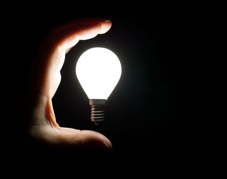 Hand grabbing floating light bulb on black background