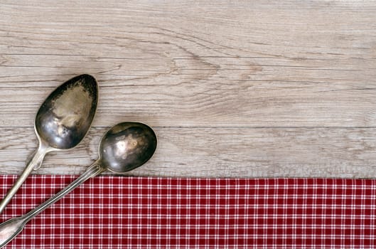 Weathered wood with two silver spoons on a red and white checkered cloth