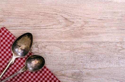 Two old silver spoons on checkered cloth and a weathered wood