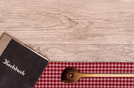 Old cookbook and wooden spoon on a cloth and board