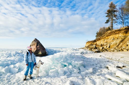 Woman with a dog walk on a sunny winter day on the coast of the sea