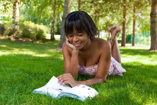 Outdoor portrait of young african american woman lying down on the grass reading a book
