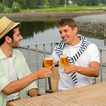 Cheerful male friends drinking beer at sidewalk pub restaurant terrace