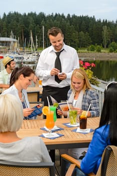 Waiter taking orders at sidewalk bar from young women