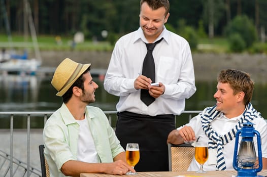 Smiling waiter taking order from men customers outdoor bar