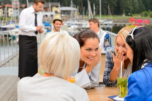 Women gossiping about men sitting at harbor bar summer terrace