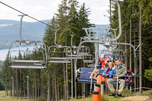 Waving young people sitting on chairlift going through forest