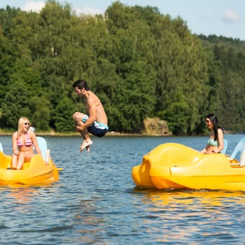 Young friends having fun jumping into water from pedal boats