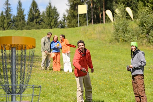 Couple throwing flying disc to chain basket at springtime park