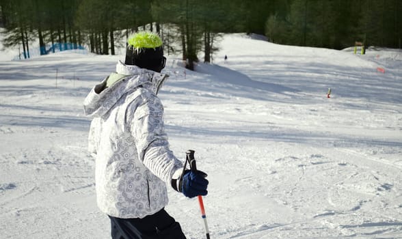 Skier or snowboarder seen from the back looking down the ski slope in sunny day