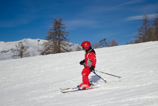 A kid in red ski suit skiing in a sunny day