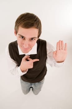 wide-angle top view of a young man in front of a white background in a white shirt and brown vestover  the hand raised in oath,looking into the camera and pointing with the right hand grinning to the left