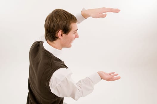 Side torso shot of a young man in jeans,white shirt and brown vestover,holding a virtual non-existent cardboard box against a white background and looking at the camera with a smile