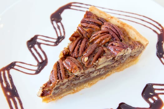 Pecan Nuts Pie with Slice with Dark Chocolate Drizzle on White Plate Closeup