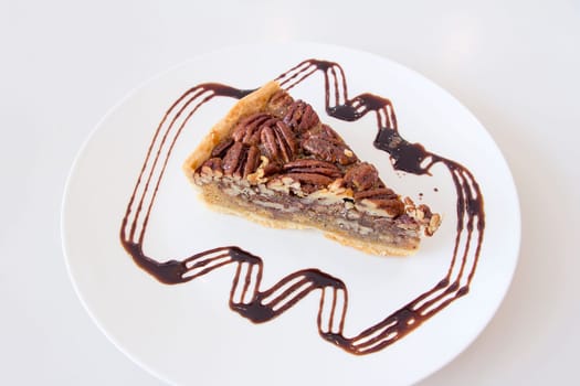 Pecan Nuts Pie with Slice with Dark Chocolate Drizzle on White Plate