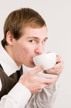 Side head and shoulders shot of a young man drinking from a white cup against a white background