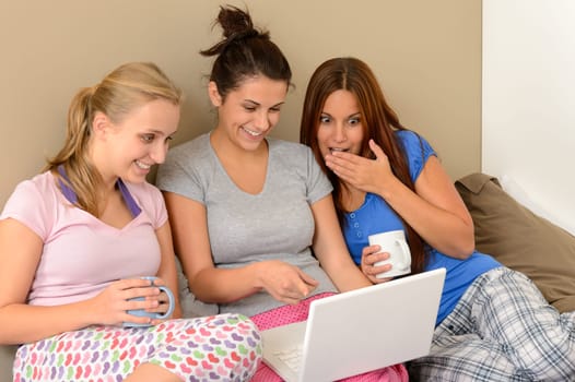 Three young girls watching movie on laptop in bed