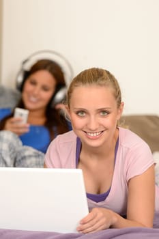 Smiling girls studying on laptop her sister listening music