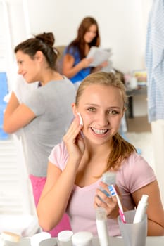 Teenage girl cleaning face with cotton pad with her friends