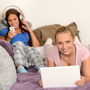 Young girls lying on bed using laptop and listening music