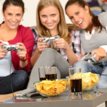 Smiling teenage girls playing with video games with potato chips