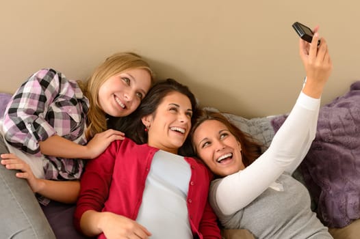 Three cheerful young girls taking picture lying on bed