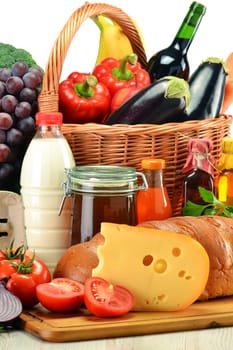 Groceries in wicker basket including vegetables, fruits, bakery and dairy products and wine isolated on white