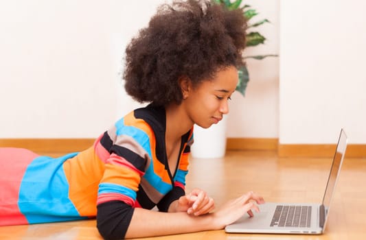 Black African American teenage girl with a afro haircut seated on the floor using a laptop computer