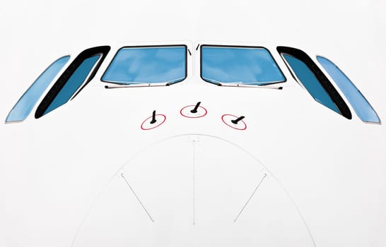 Close up front view of pilot cabin of modern jumbo jet. White plane with blue windows. Lots of copy space.