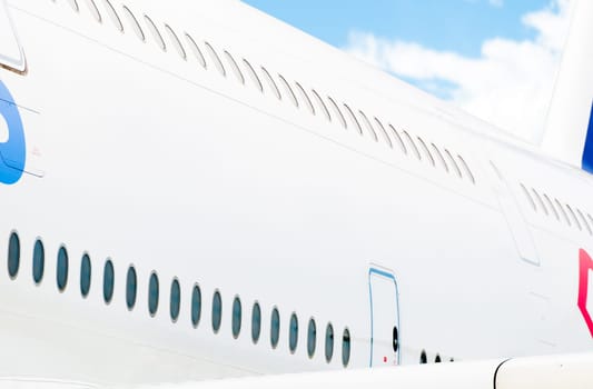 Side view of white passenger plane with two rows of windows and blue cloudy sky in background. Place for copy.