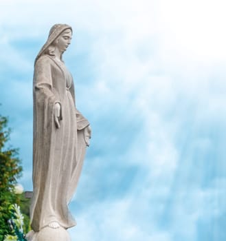 Beautiful stone statue of woman. Blue cloudy sky in background. Sun with sun rays.