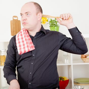 Man standing lost in thought while cooking in the kitchen absent mindedly scratching the back of his head with a wooden spoon