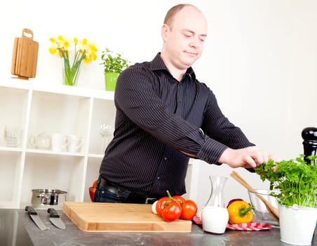 Man picking fresh herbs from a potted plant while standing in a clean white kitchen preparing a meal with fresh vegetables