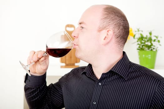 Man standing sideways to the camera enjoying a glass of red wine sipping elegantly from a wineglass